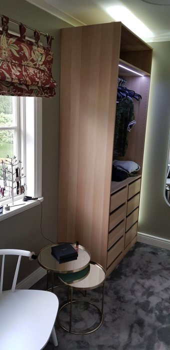 Omvandlat barnrum till walk-in closet med öppet garderobssystem, lådor och sittplats vid fönster.