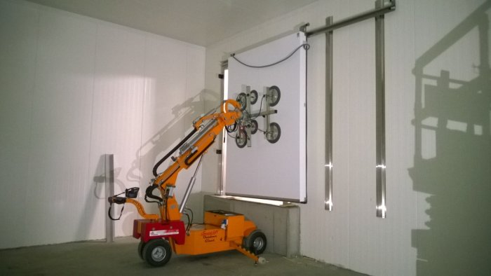 Lyftkran för dörrar i användning, håller en vit 150 kg tung dörr vertikalt inne i en byggnad.