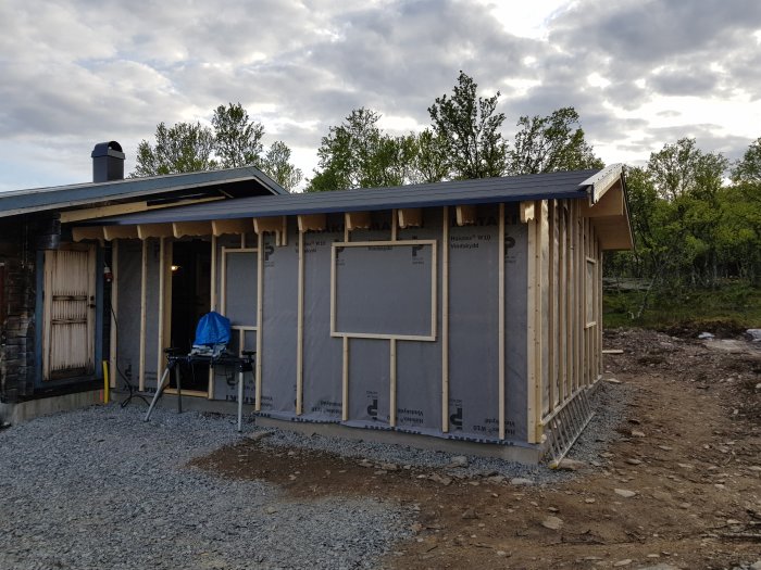 Nybyggt hus med tak, plåtar, vindskivor och påbörjad vindduk i dagsljus.