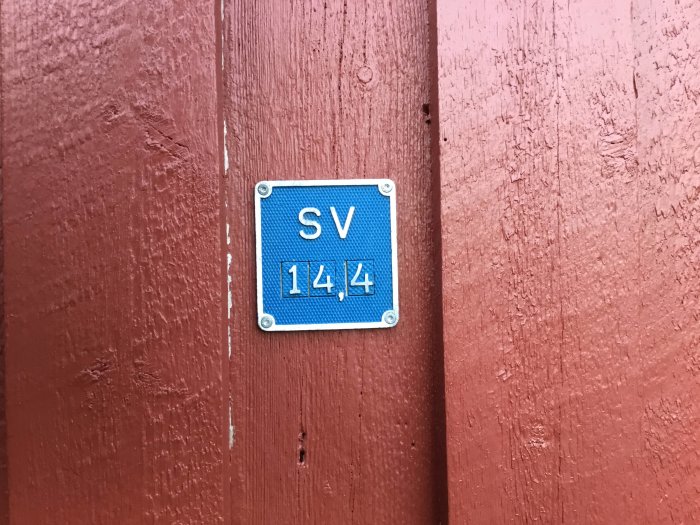 Nyrenoverad blå skylt med texten "SV 1414" på en rödmålad trävägg.