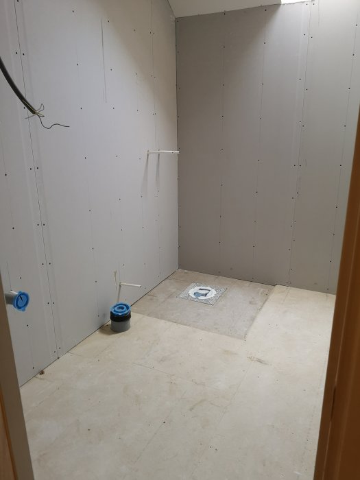 Ej färdigställt badrum med gipsskivor på väggar och osatt golv redo för mattläggning.