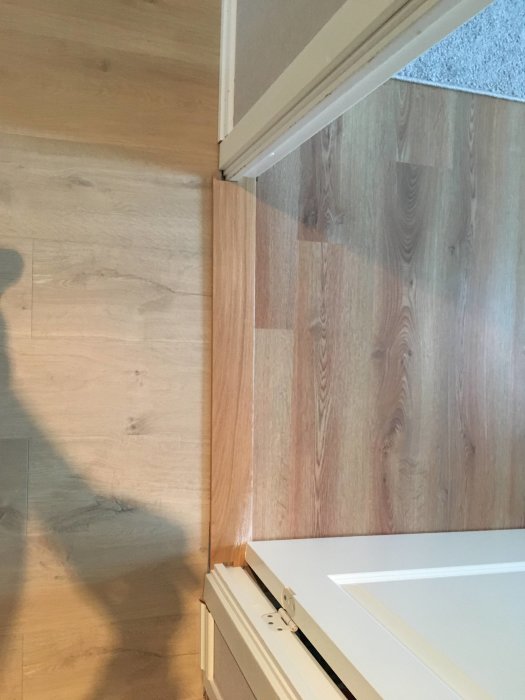 Laminatgolv möter tröskel utan list, vid en stängd vit dörr och dörrkarm, med 7 mm mellanrum under dörren.