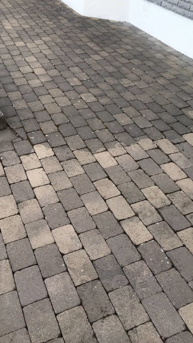 Stenbelagt garageuppfart med märken och smuts före högtryckstvättning.