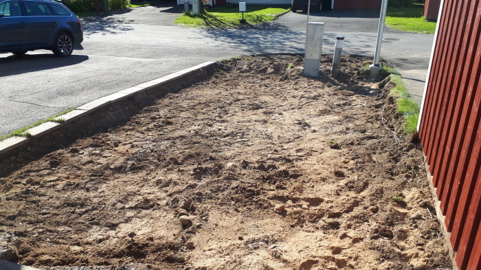 Schaktad mark vid altan förberedd för tillbyggnad, med synlig jord och gräsmattans kanter.