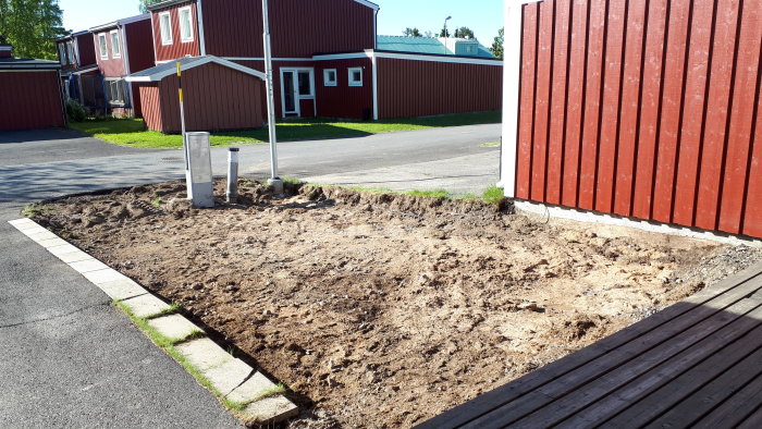 Uppgrävd yta för tillbyggnad av altan med synligt schaktat gräsmarksområde och angränsande bostadshus.