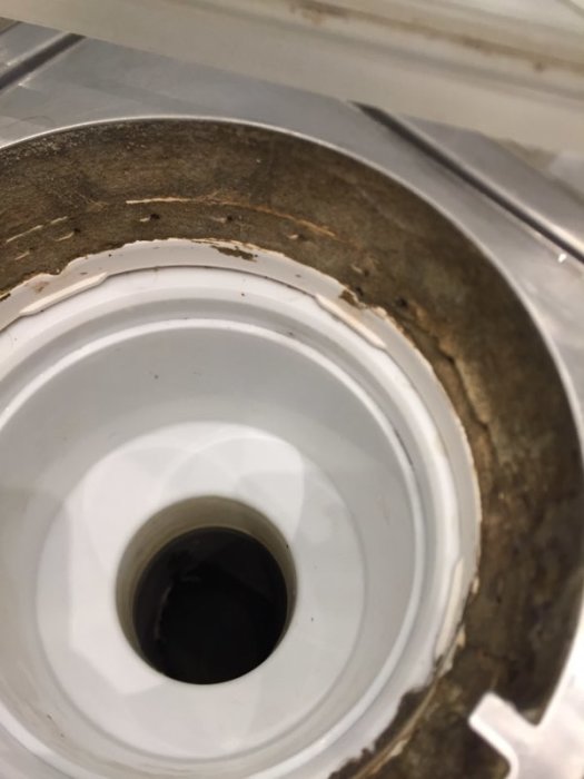 Närbild på en badrumsgolvbrunn som visar tecken på möjlig fukt med rost och smutsiga kanter.
