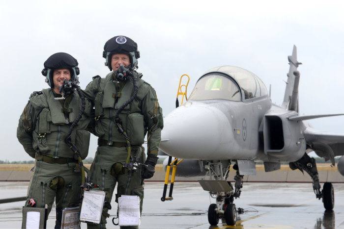 Två piloter i flygdräkt står framför en stridsflygplan "JAS 39 Gripen".