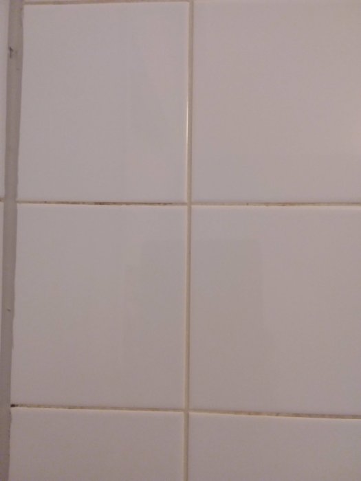 Vägg med kakelplattor och missfärgad fog som behöver rengöras eller bytas.