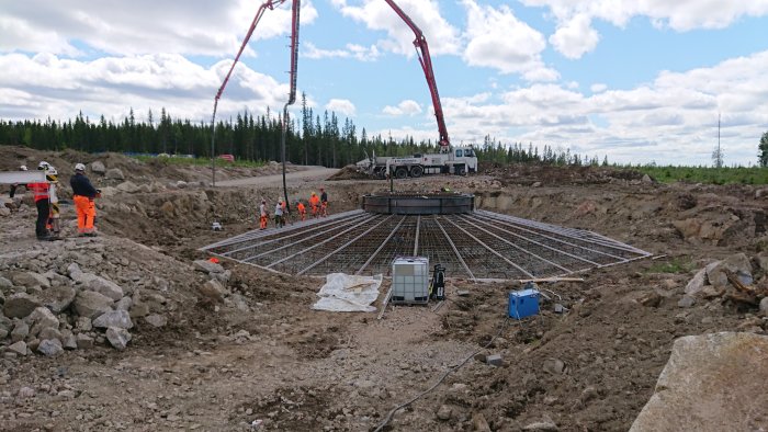 Arbetsplats med armeringsjärn och betongpump vid stort gjutningsprojekt, arbetare i säkerhetskläder syns.