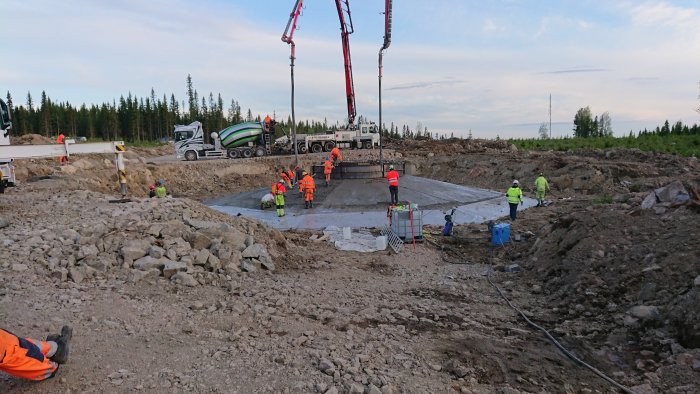 Arbetare häller betong i bygggrund med hjälp av betongpump och betongbil på byggarbetsplats.