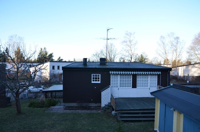 Ett hus före solpanelinstallation med ett platt svart tak, antenn och träveranda.