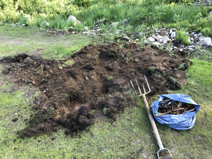 Uppgrävd gräsmatta med synligt rotsystem, grepe och en säck med trädgårdsavfall.