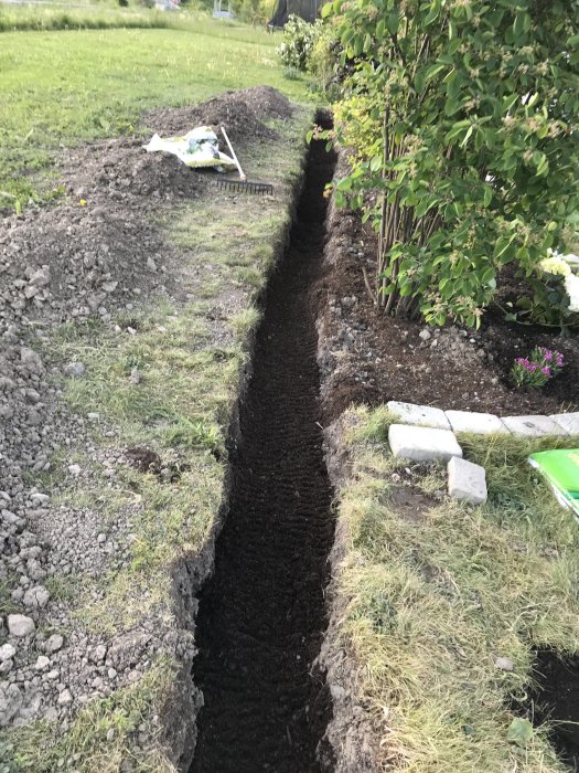 Grävt dike i trädgården fyllt med mörk planteringsjord för thujaplantation, kratta och säck på marken.