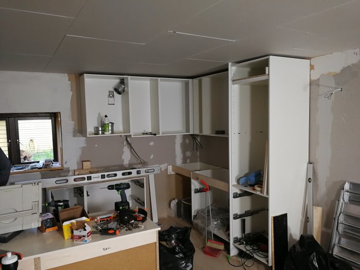 Kök under renovering med delvis monterade skåp och nytt innertak, verktyg och material utspridda på arbetsytor.