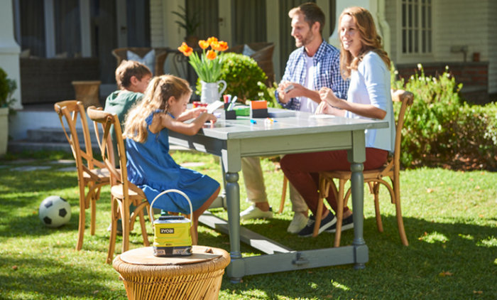 Familj sitter vid utebord med Ryobi myggskydd på bord i trädgård.