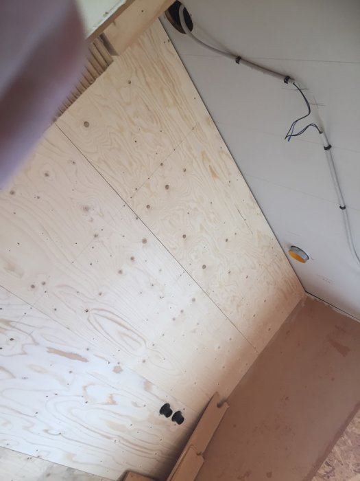 Nyinstallerat plywoodgolv med utstickande elkablar och genomföringar i en byggmiljö.