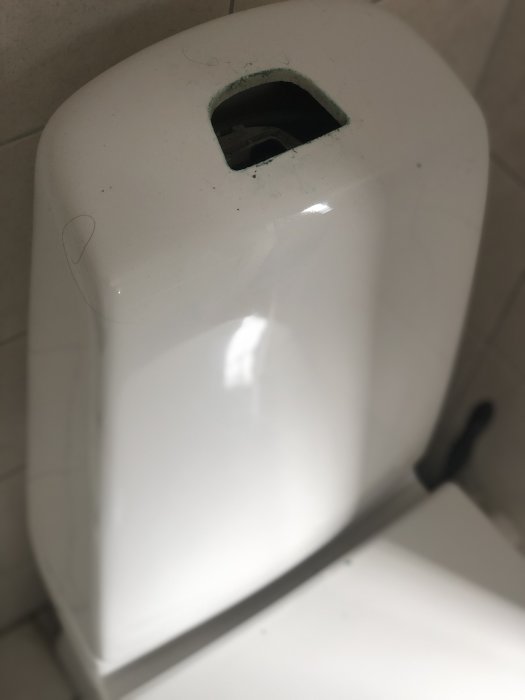Vit toalettens övre del med avlägsnade knappar och synlig intern mekanism genom hålet.
