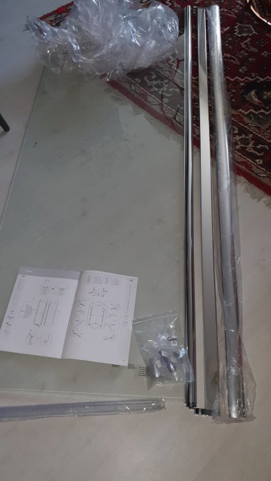 Opackad duschväggssats från Basano på ett golv med monteringsinstruktioner och skruvförpackningar.