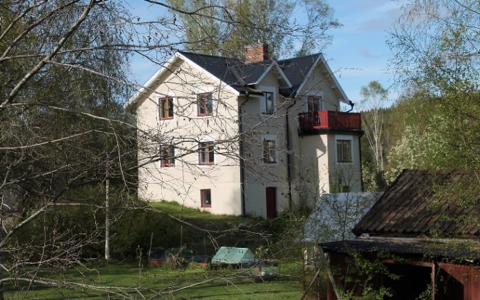 Vitt hus av slaggsten från 1800-talet omgivet av grönska i Bergslagen.