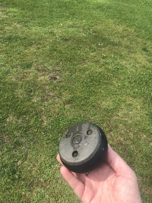 Hand håller ett förlorat hjul från en automatisk gräsklippare, med gräsplan i bakgrunden.