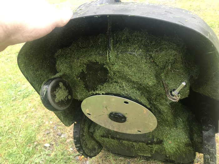 Omvänd robotgräsklippare med saknat framhjul och synlig gräsklipp under.