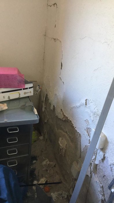 Vägg i garage med flagnande plastfärg och synligt underliggande murverk.