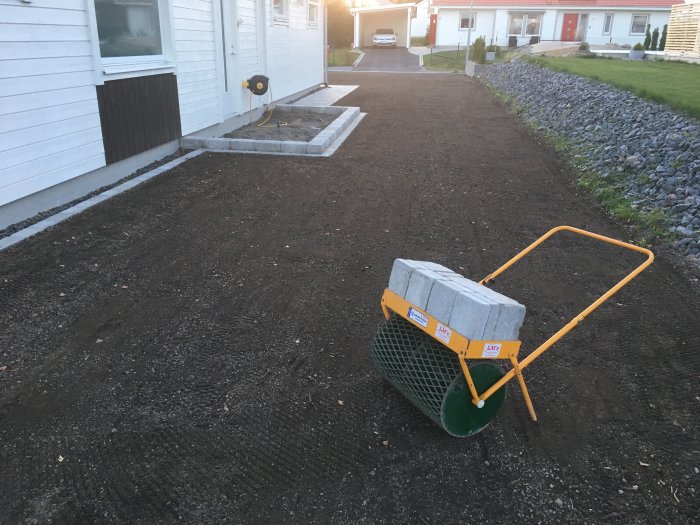 Nyplanterad gräsmatta med synligt grus och en skottkärra full med trottoarstenar.