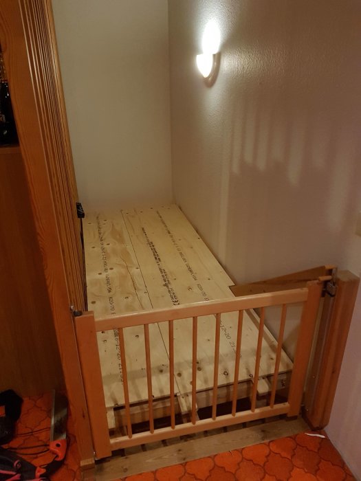 En hemmagjord plattform av en sågad lastpall och byggplywood som vilar på träreglar, placerad vid en trappa.