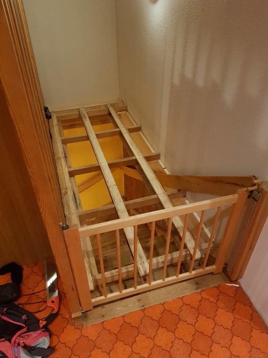 En hemmagjord träplattform konstruerad av en avsågad lastpall och träreglar för att nå väggar nära en trappa.