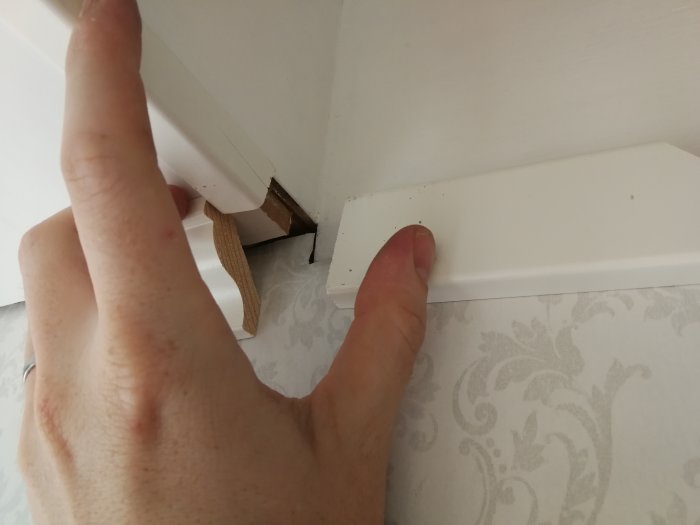 Hand som håller emot tre olika lister som möts i ett hörn vid trappans nedre del.