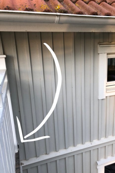 Utzoomad bild av en grå panelvägg på ett hus med ett fönster och takränna, med vit markering.