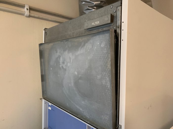 Öppnad frontlucka på en kompressor med isoleringsskiva och dammiga inre delar synliga.