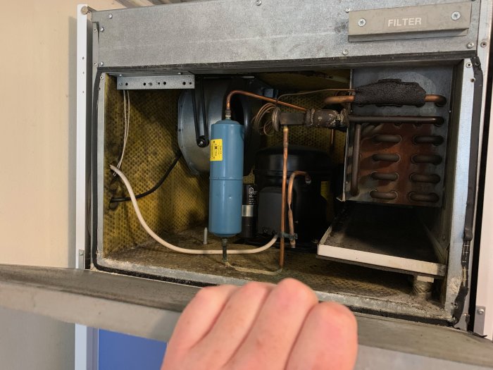 Öppen kompressordel på värmepump med synlig fläkt, filter och isolering.
