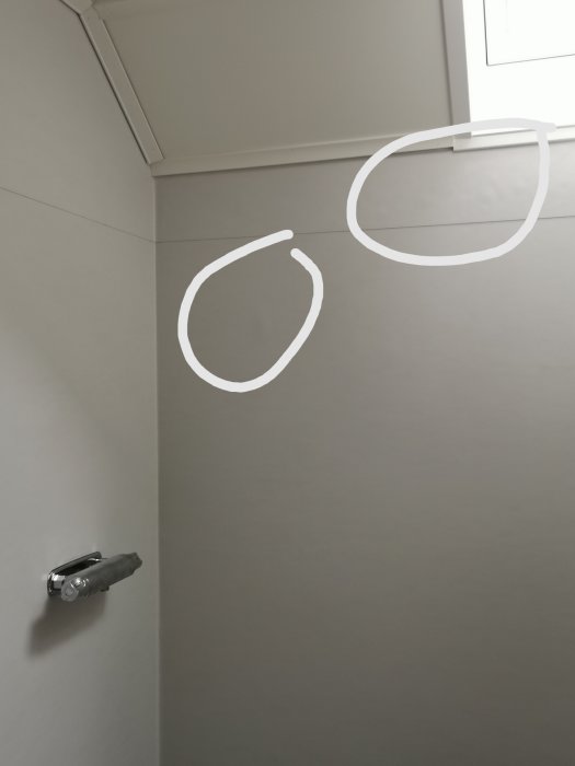 Hörn av ett rum med gråa väggar, där vita cirklar är ritade för att markera specifika ställen.