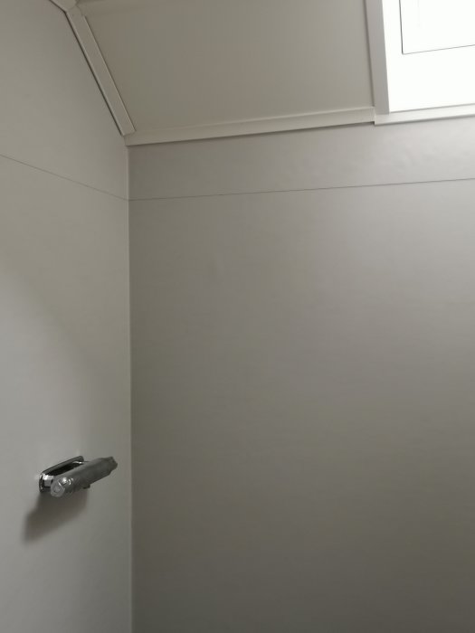 Interiör av hörn i rum med takfönster och vägglampa, utan markeringar.