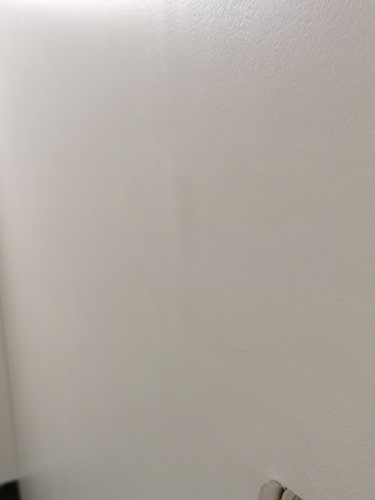 Vit målad vägg med svagt synlig defekt nära hörnet, ej markerad.
