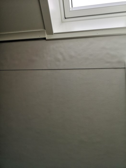 Interiörbild som visar en vägg under ett fönster, markeringsring saknas för att identifiera specifikt ställe.