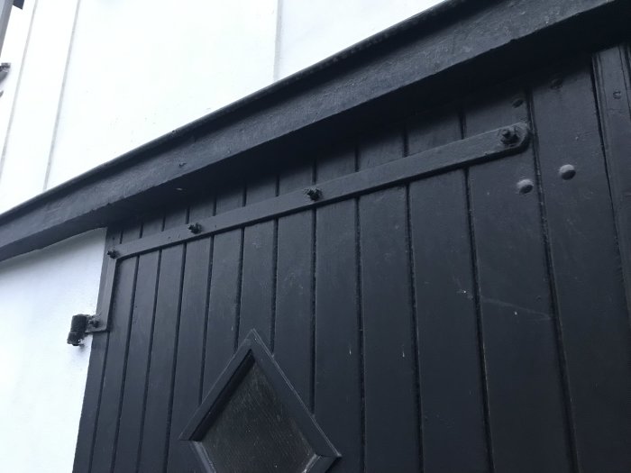 Övre delen av en gammal svart garagedörr med järnbeslag från 1927 i gott skick.