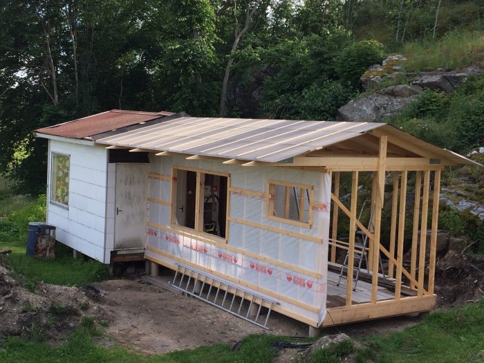Påbörjad tillbyggnad av trä till en befintlig stuga, med takstolar och vindskydd installerat.