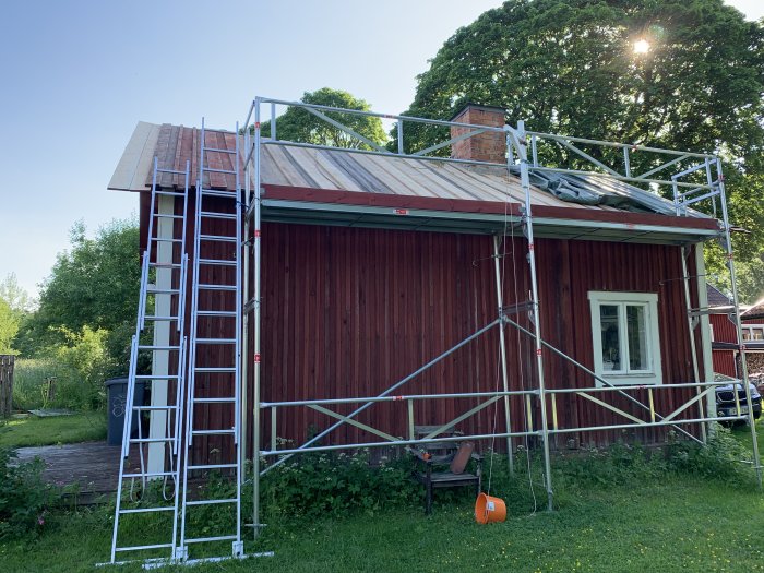 Renoveringsarbeten på ett rött trähus med byggställning, oavslutat tak och skorsten.