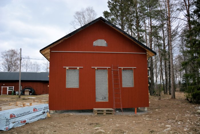 Nybyggt rött fritidshus med pågående panelarbete och uppsatt stege mot vägg.