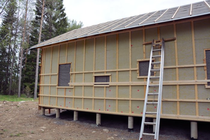 Fritidshuset under renovering med pågående panelarbete på ena långsidan och en stege lutad mot väggen.