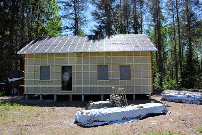 Fritidshus under konstruktion med omonterad panel och byggmaterial i förgrunden.