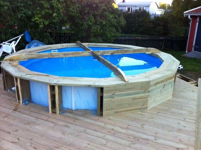 Rund uppbyggd pool med blått vatten och träkors ovanpå för att förhindra överdraget från att sjunka ner och samla vatten.
