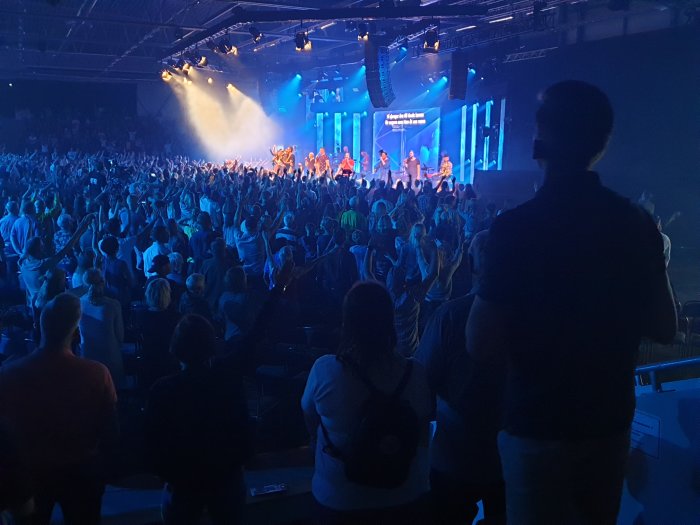 Publik som ser på en liveföreställning i en mörk konserthall.