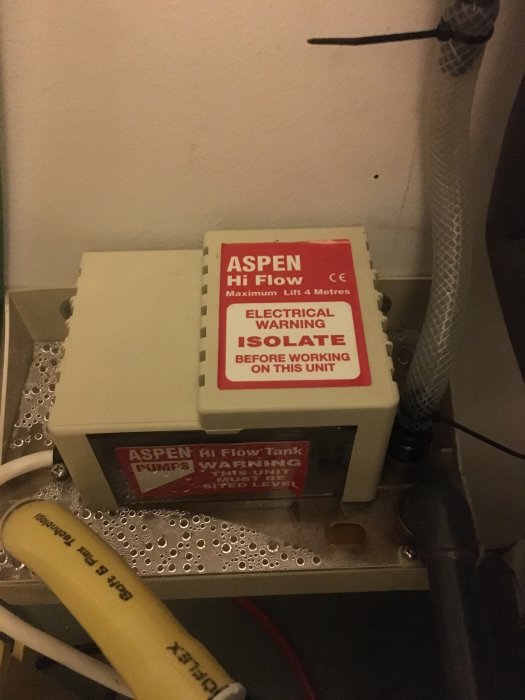 Mörkgrått rör nere till höger som leder till en Aspen Hi Flow kondensvattenpump, omgiven av varningsetiketter och rör.