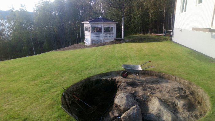 En grävd grop för en blivande pool med en skottkärra och stenblock vid en villa med lusthus.