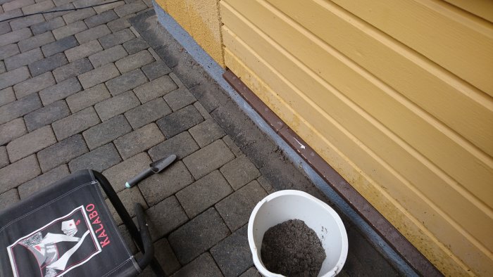 Marksten med pågående fogbyte till hårdfog, trädgårdsredskap och hink med fogsand.