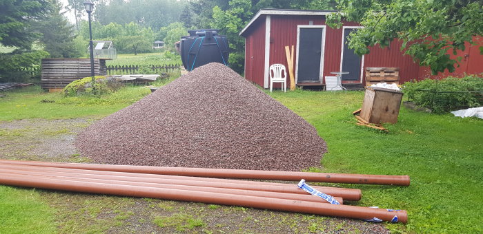 En stor hög av 8-16 makadam med flera orange markrör framför på gräsmatta, nära en röd stuga.