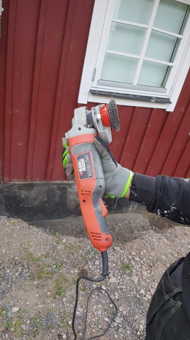 Person använder en vinkelslip med stålborste för att ta bort tjära från en källarvägg.